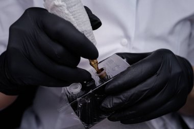 Dövme makinesini tutan ve pigmenti ona çeviren ustanın ellerine yakın çekim. PMU Prosedürü, Kalıcı Kaş Makyajı.