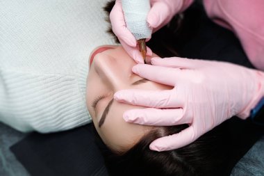 Usta, kirpiklerin arasında kalıcı makyaj yapmak için göz kapağını parmaklarıyla çeker. Kalıcı göz makyajı ve PMU kirpikleri.