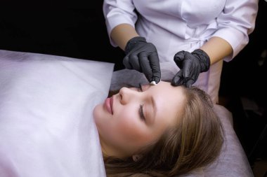 Usta kremi bir pamuk sünger kullanarak modelin kaşlarına sürüyor. PMU Prosedürü, Kalıcı Kaş Makyajı.