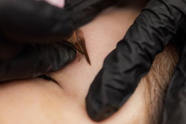 Kalıcı kaş makyajının düzeltilmesi için usta dövme makinesinin ellerinde. Bir ay içinde kalıcı kaş makyajı yapılan ikinci PMU prosedürü. Kalıcı makyaj düzeltmesi.