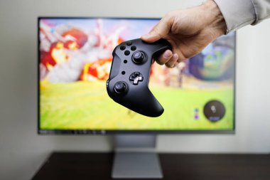 Elimdeki monitörün önünde bir video oyun kumandası var. Video oyunu oyun sahası elinde