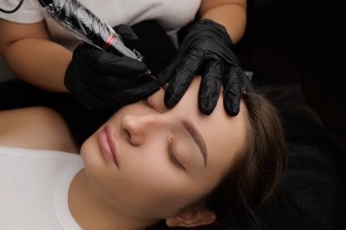 Kaş manzarasının kalıcı makyajını üstten yapan ustanın ellerine yakın çekim. Esmerler için kalıcı kaş makyajı PMU