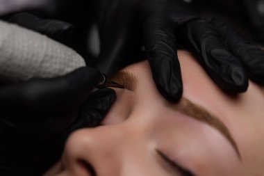 Kalıcı makyaj sanatçısının ellerinde kaşına dövme uygulamak için bir araç sanatçı kaşlarına dövme uygular. Kalıcı kaş makyajı, PMU için kahverengi pigmentli kaş dövmesi..