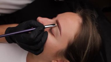 Kaşlarını fırça ve boya kremiyle kaplıyor. Açık renk kaş makyajı, kaş dövmesi.