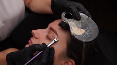 Usta göz kapaklarına nazikçe renkli krem sürüyor. Açık renk kaş makyajı, kaş dövmesi.