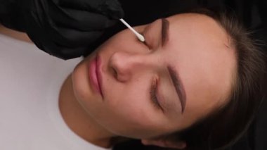 Efendinin kirpikleri temizlediği kozmetoloji kanepesinde gözleri kapalı bir kız. Açık renk kaş makyajı, kaş dövmesi.