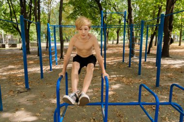 Genç bir çocuk egzersiz yaparken bacaklarını kaldırarak kaslarını özenle zorluyor. Parkta spor yapan genç bir çocuk. 