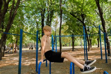 Antrenmandan sonra, genç bir çocuk merminin tepesinde rahatça oturur. Parkta spor yapan genç bir çocuk. 