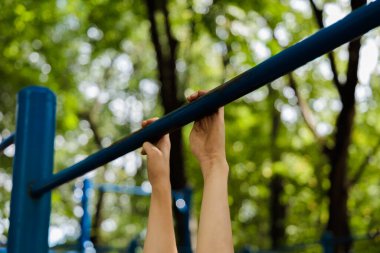Çapraz demiri tutan sporcunun ellerine yakın çekim. Parkta spor yapan genç bir çocuk. 