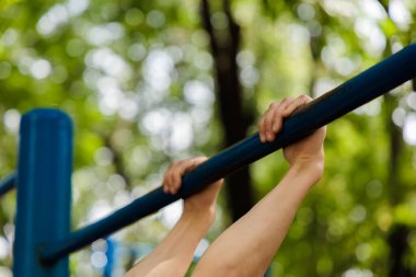 Çapraz demiri tutan sporcunun ellerine yakın çekim. Parkta spor yapan genç bir çocuk. 