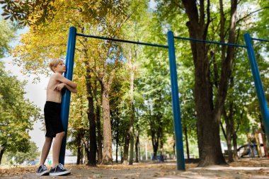 Antrenmandan sonra yorgun düşen bir genç ayakta durur ve dinlenir. Parkta spor yapan genç bir çocuk. 