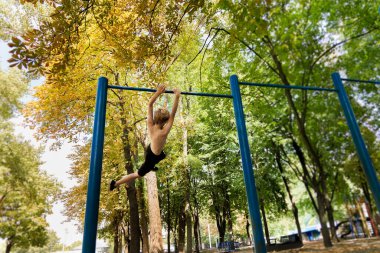 Dışarıda çalışan bir çocuk barda numaralar yapıyor. Parkta spor yapan genç bir çocuk. 