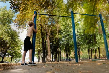 Antrenmandan sonra yorgun düşen bir genç ayakta durur ve dinlenir. Parkta spor yapan genç bir çocuk. 