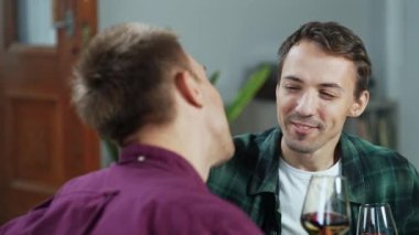 Mutlu, gülümseyen homoseksüel genç adamın sevgili ortağını öptüğü ve romantik bir randevu sırasında birlikte şarap içtiği portresi. Sevgi dolu eşcinsel çift birlikte mutlu anlar yaşıyor.. 