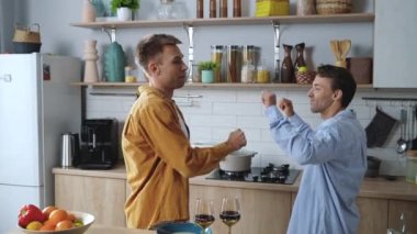 Cheerful smiling gay couple having fun and dancing on the kitchen, while celebrating. Happy young homosexual males enjoying staying at home. High quality 4k footage