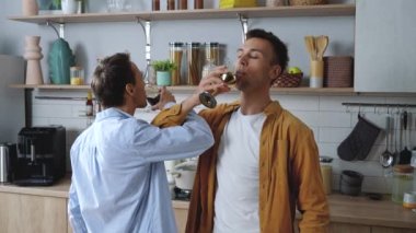 Authentic shot of young happy homosexual male gay couple drinking wine on brotherhood and kissing, while dancing on the kitchen at home.