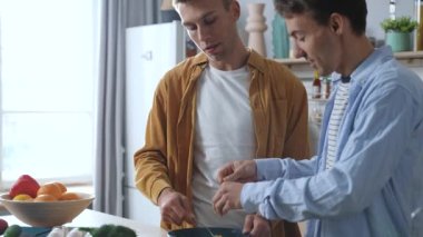 Portrait of same-sex couple preparing breakfast together at the kitchen. Romantic young homosexual men spending time together cooking dishes. LGBT concept. High quality 4K footage