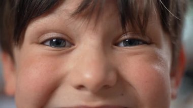 Güzel gri-mavi gözleriyle kameraya bakan sevimli, gülümseyen beyaz bir oğlanın yakın çekimi. Ağır çekim. Yüksek kalite 4k görüntü.