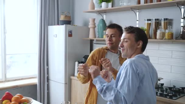 无忧无虑的年轻男同性恋们庆祝周末 庆祝搬家日 同时在舒适的厨房里欢快地跳舞 快乐的夫妇在做饭的时候玩得很开心 高质量的4K镜头 — 图库视频影像