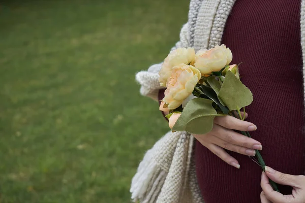 Elinde bir buket çiçekle hamile bir kadının göbeği. Beyazlı doğal yün bir battaniyesi var..