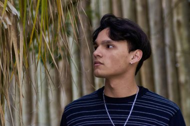 Siyah beyaz çizgili gömlekli ve gümüş kolyeli bir adam ayakta duruyor. Çocuğun profili var, geçmişi bulanık..