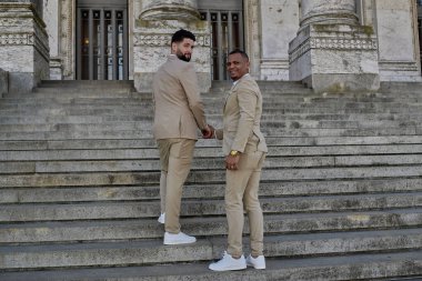 Merdivenleri tırmanan iki adam, LGBT topluluğundan eşcinsel bir çift. İkisi de şık giyinmiş.