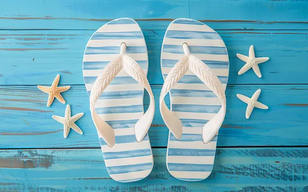 Mavi tahta üzerinde mavi ve beyaz çizgili plaj sandaletleri. Sahneyi dört denizyıldızı süslüyor, sandaletlerin her iki tarafında da iki tane. Yaz ve tatil temaları için ideal.