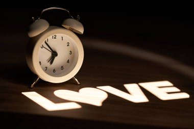 Retro tarzı alarm saati, komodindeki aşk sözcüğüyle aydınlatılmış.