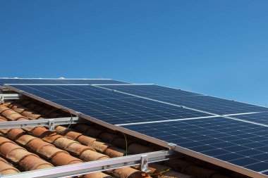 Kırmızı çatıdaki güneş paneli güneşi ve arkadaki bulutlu mavi gökyüzünü yansıtıyor. Yüksek kalite fotoğraf