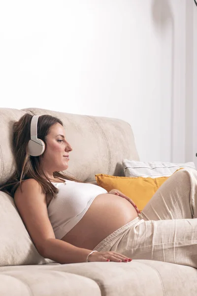Genç Hamile Bir Kadın Evdeki Kanepede Dinlenirken Kulaklıkla Müzik Dinliyor — Stok fotoğraf