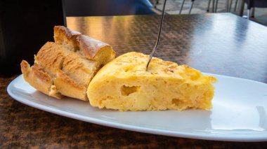 Yeni hazırlanmış bir İspanyol omleti büyüleyici bir açık hava kafede bir dilim kabuklu ekmeğin yanında servis edilir. Sıcak güneş ışığı öğle yemeği için mükemmel bir yemek atmosferi yaratır..