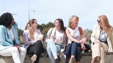 Beş kadın birlikte oturmuş, açık bir alanda açık mavi gökyüzünün altında canlı bir sohbet ve içeceklerin keyfini çıkarıyorlar. Bu, arkadaşlığı yansıtan canlı bir an..