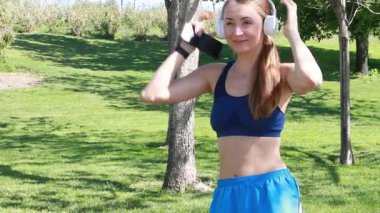 Dışarıda ayakta dururken kulaklıkla müzik çalan kadın koşucunun yavaş çekimleri. .