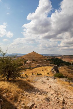 İspanya, Atienza, Guadalajara 'yı çevreleyen kayan tepelerin manzarası, açık hava keşfi ve fotoğrafçılık için mükemmel, parlak bir gökyüzü altında antik kalıntıları ve çimenli araziyi gösteriyor..