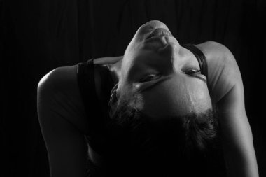 Siyah tişörtlü genç bir kadının siyah beyaz stüdyo resmine karşı siyah stüdyo arkaplanı. Stüdyoda duruyor..