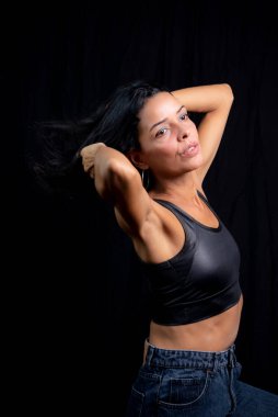 Studio portrait of young woman in black t-shirt against plain black studio background. She standing in the studio.