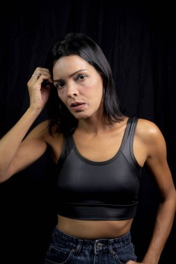 Studio portrait of young woman looking at camera against simple studio black background. She wears a black t-shirt.