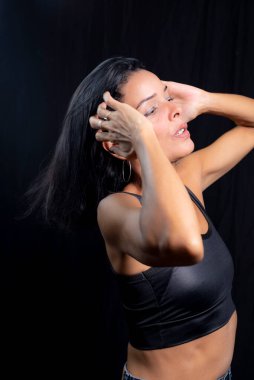 Studio portrait of young woman in black t-shirt against plain black studio background. She standing in the studio.