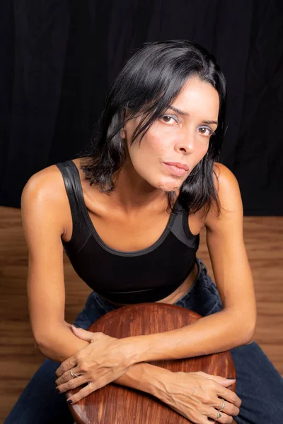 スタジオ黒いスタジオの背景と木製の床に対して カメラを見て黒いTシャツの若い女性の肖像画 ブラジルのサルバドール — ストック写真