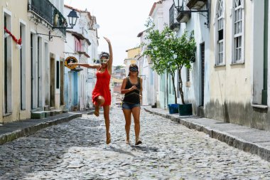 İki güzel ve mutlu kızın parke taşı caddede zıplayan portresi. Salvador, Brezilya 'daki Pelourinho caddeleri.