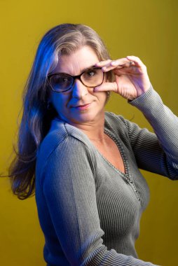 Sarı arka planda gözlük takan bir model portresi. Bardakları manipüle ediyor. Sakin kadın..