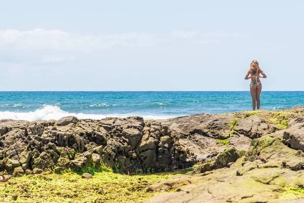 Salvador, Bahia, Brezilya - 26 Ekim 2019: Bikinili genç bir kadın Pedra do Sal sahilinin kayalıklarında denize bakıyor. Salvador, Brezilya.