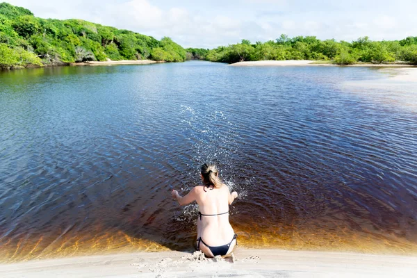 Woman Bikini Sitting Bank River Splashes Water Upwards Forest Sky — Stok fotoğraf