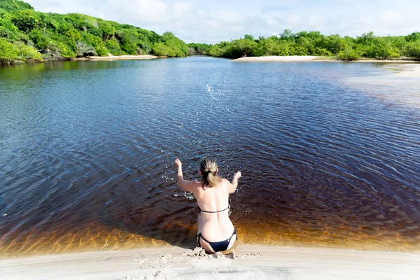 Woman Bikini Sitting Bank River Splashes Water Upwards Forest Sky — Stok fotoğraf