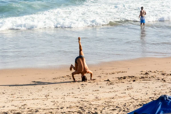 巴西巴伊亚州萨尔瓦多市 2022年10月22日 一名男子在巴西萨尔瓦多法罗达巴拉海滩的沙滩上做瑜伽练习 而其他人则在旁边走过 — 图库照片