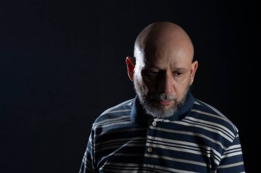 Sakallı, yakışıklı ve kel bir adam siyah arka plan üzerine sıradan bir gömlek giyiyor. Endişeliyim. Düşünceli..