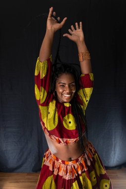 Siyah arka planda renkli uzun elbiseler giyen genç bir kadın. Doğal ifade.