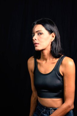 Studio portrait of young woman looking at camera against simple studio black background. She wears a black t-shirt.