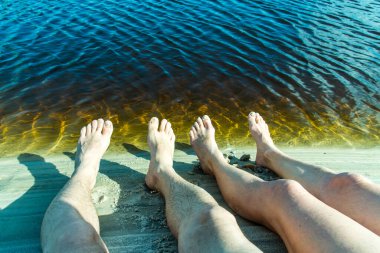 Legs of a man and a woman by the river against reddish water in the background. Guaibim beach in the city of Valenca, Bahia, Brazil.