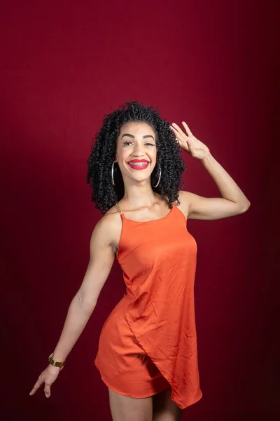 若い美しい笑顔の女性 立って スタジオで赤を背景にオレンジ色の服を着て — ストック写真